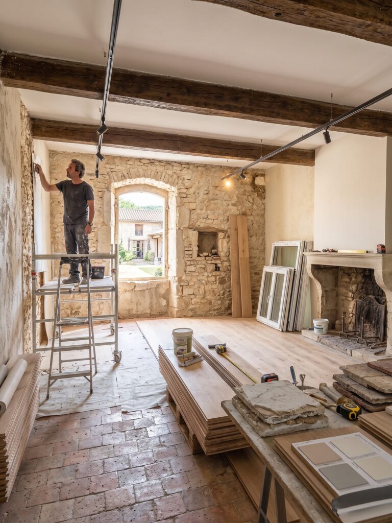 Artisan sur un échafaudage dans une pièce en rénovation avec murs en pierre et poutres apparentes