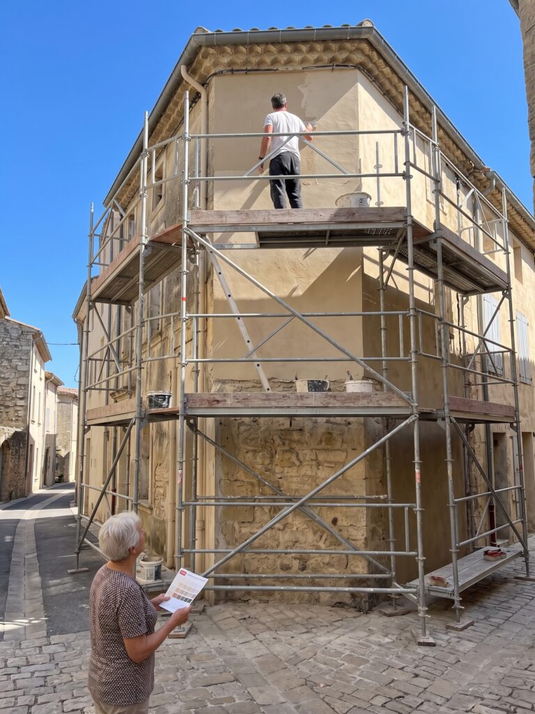 Échafaudage autour de la façade d’une maison dans une rue pavée, avec un artisan en hauteur