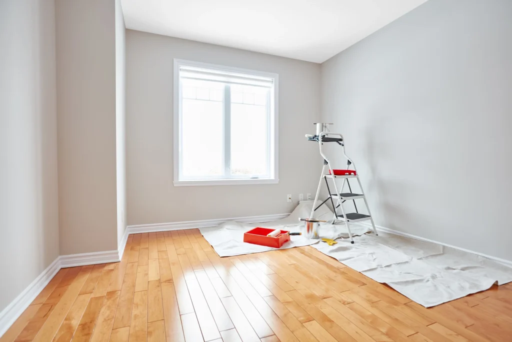 Pièce aux murs clairs avec escabeau et matériel de peinture sur un parquet protégé