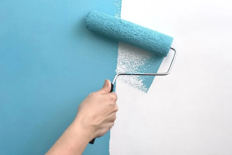 Main appliquant de la peinture bleue au rouleau sur un mur blanc