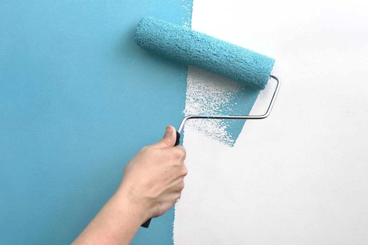 Main appliquant de la peinture bleue au rouleau sur un mur blanc