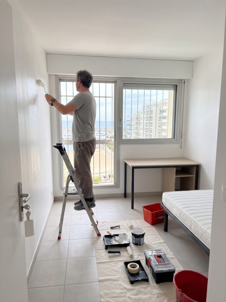 Artisan sur un escabeau peignant un mur dans une chambre