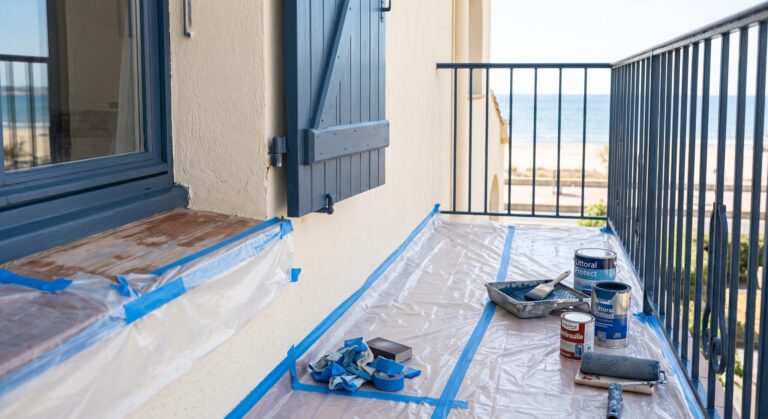 Balcon avec volets bleus, garde-corps et matériel de peinture face à la mer