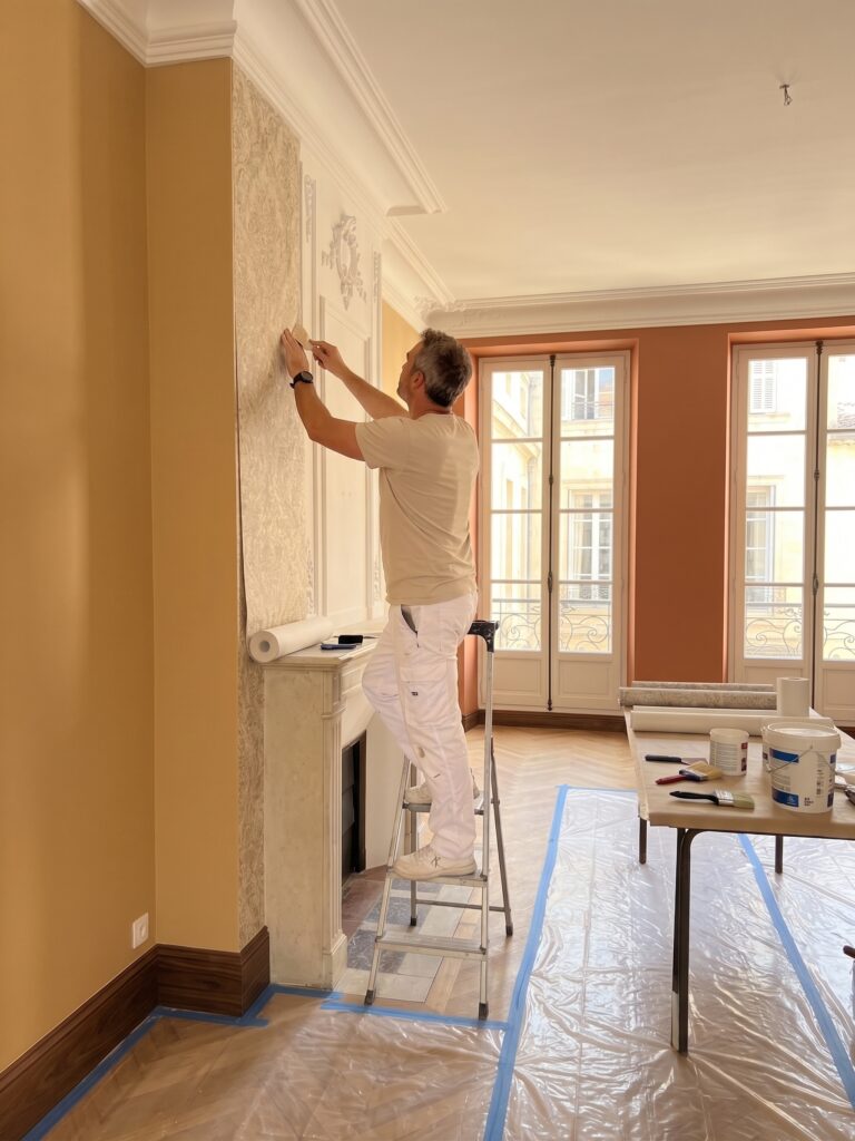 Artisan sur une échelle posant du papier peint dans une pièce