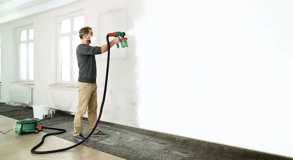 Peintre appliquant une peinture au pistolet sur un mur blanc