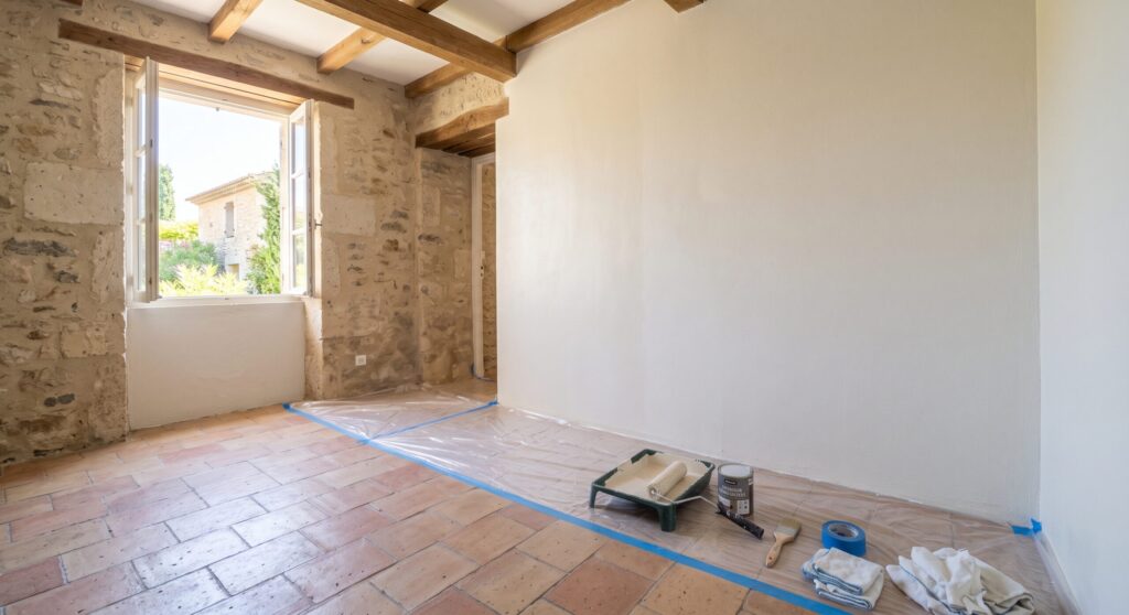 Mur clair dans une pièce aux murs en pierre et poutres apparentes, avec matériel de peinture
