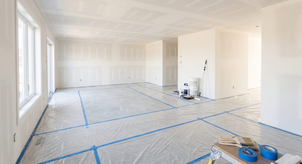 Grande pièce avec joints de plaques de plâtre visibles aux murs et au plafond, sol protégé