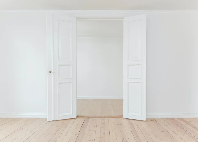 Pièce aux murs clairs et au parquet bois avec portes doubles ouvertes