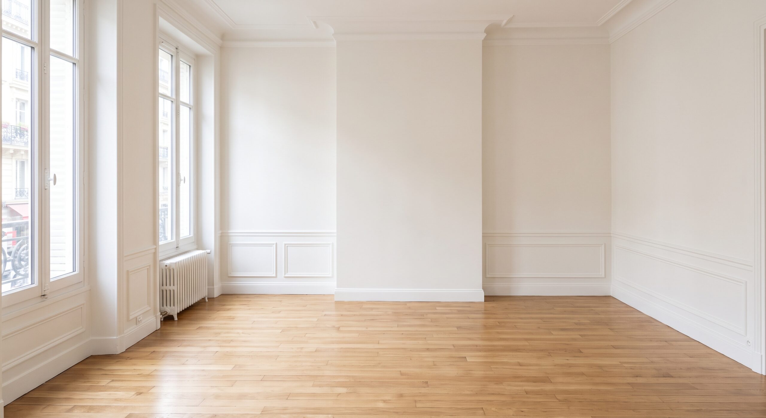 Pièce vide aux murs clairs, avec moulures, soubassements et parquet